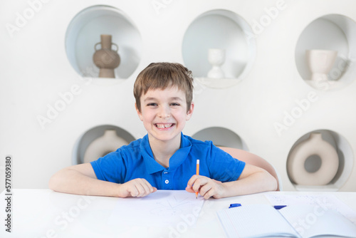 Cute and happy school boy sits at the desk and learns his lessons