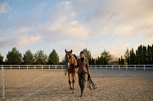 Woman rider walking horse side by side holding harness saddle-girth photo