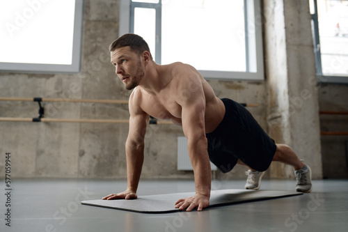 Fototapet Young athletic man doing push-ups physical workout in gym
