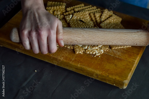 hands that break biscuits with a rolling pin to prepare the crunchy base of a cheesecake