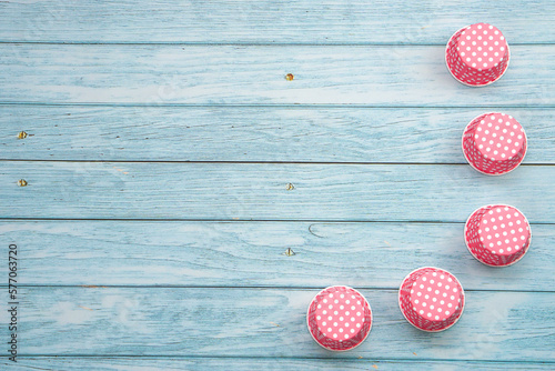 Pink polka dot cupcake cases on blue wooden floor.  Materials or kitchen equipment for bakery.