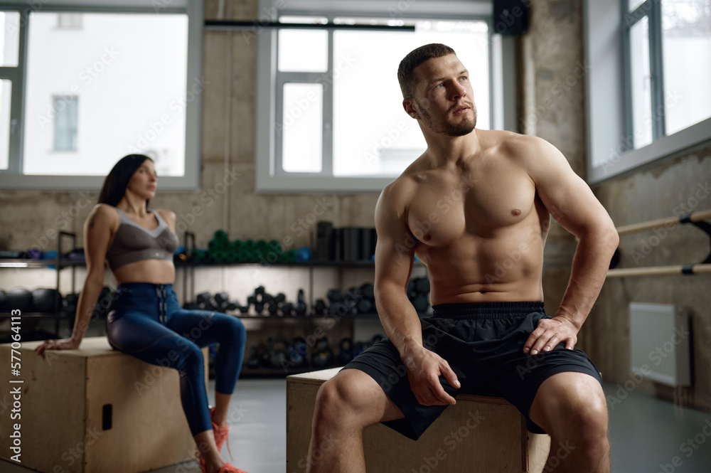 Obraz premium Portrait of young adult sports people having rest while sitting on fitness box