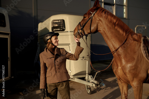 Young adult smiling rider woman stroking horse nose