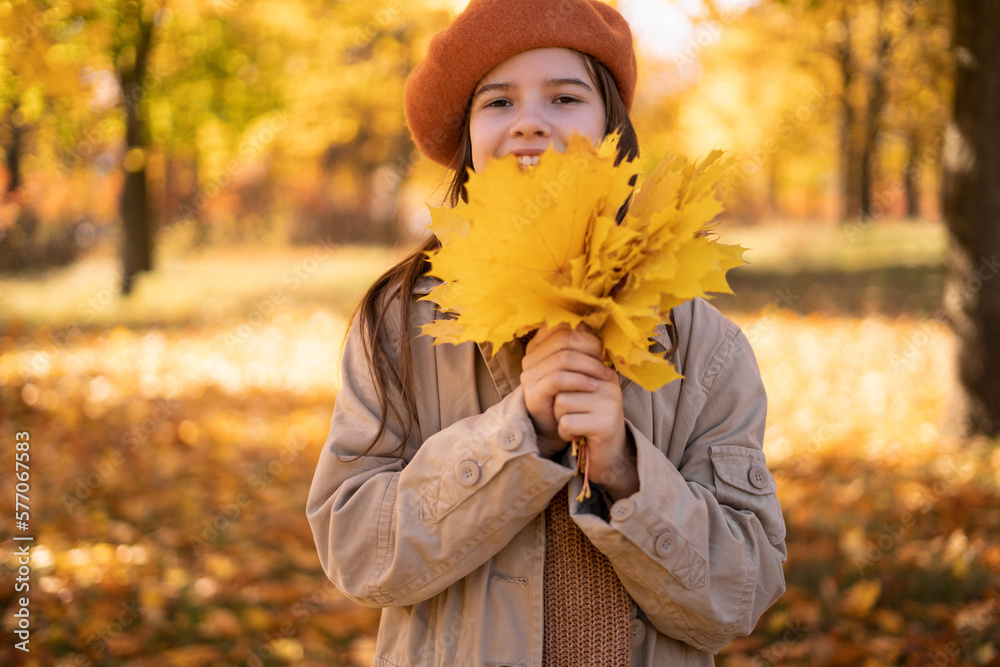 Beautiful autumn girl child with autumn leaves on fall nature background. Teen girl holding autumn leaves and smiling outside in colorful fall forest.