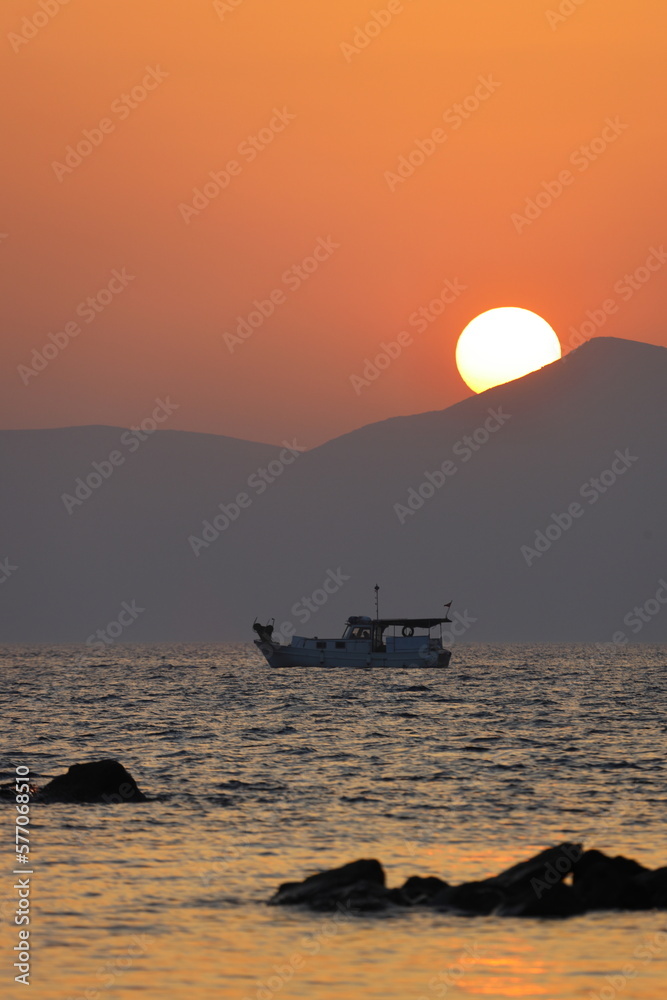 a lonely fishing boat in the sea as the sun sets behind the mountains