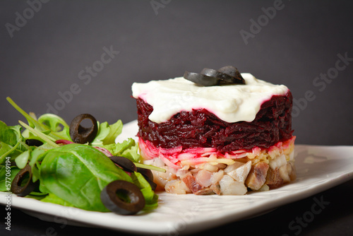 Side view of Norwegian layered fish salad Herring under fur coat. Portion with marinated herring, onion, grated potato, beetroot, mayonnaise on top with lettuce olive salad. Dark copy space background