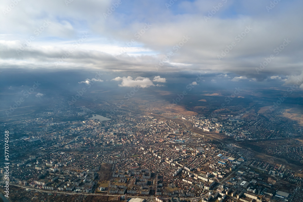 Aerial view from high altitude of distant city covered with puffy cumulus clouds flying by before rainstorm. Airplane point of view of landscape in cloudy weather