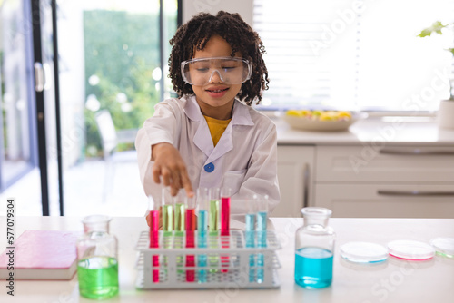 Cute smiling hispanic boy wearing protective eyewear doing scientific research with chemicals photo