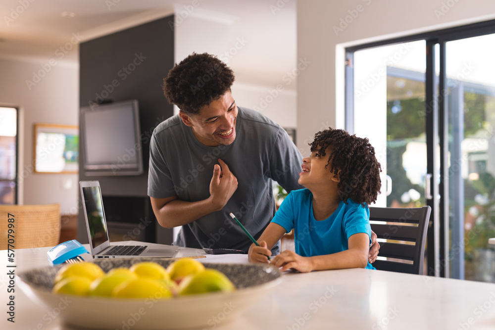 Happy hispanic father and son talking while doing homework in kitchen at home Happy hispanic father and son talking while doing homework in kitchen at home
