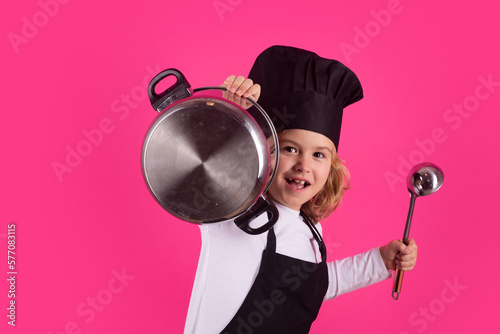 Fynny kid chef cook with cooking pot and ladle. Child in cook uniform. Chef kid isolated on pink background. Cute child to be a chef. Child dressed as a chef hat. photo