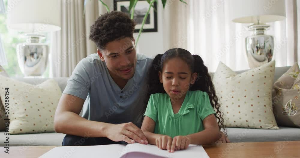 Happy biracial father and daughter sitting on sofa reading braille Happy biracial father and daughter sitting on sofa reading braille