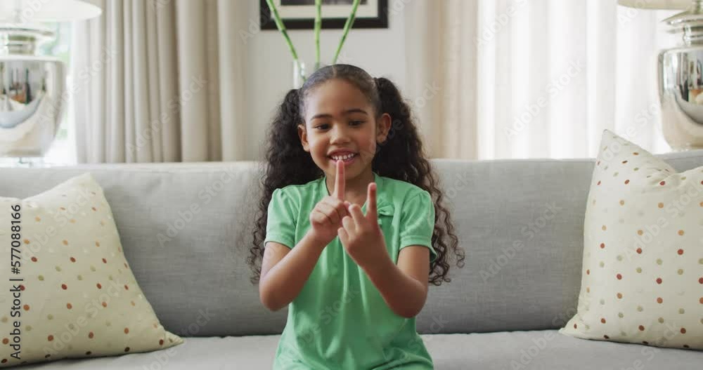 Happy biracial girl sitting on sofa using sign language Happy biracial girl sitting on sofa using sign language
