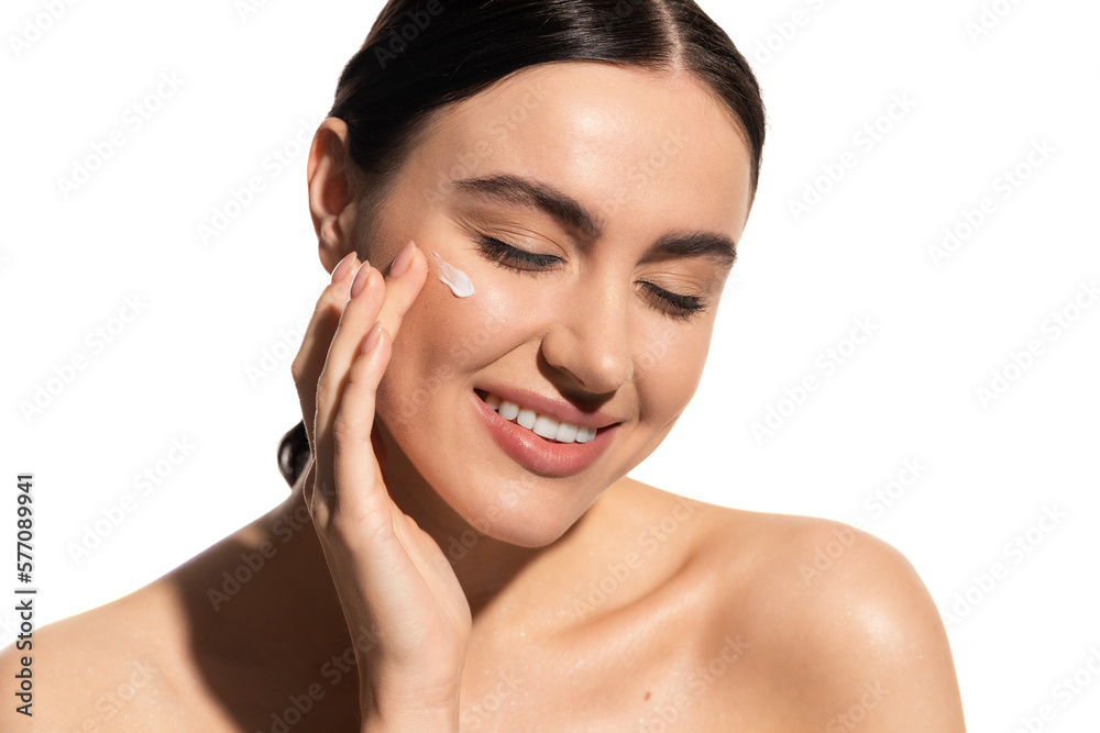 satisfied young woman applying moisturizing face cream on cheek isolated on white.