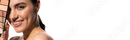 positive young woman covering eye with eye shadow palette isolated on white, banner.