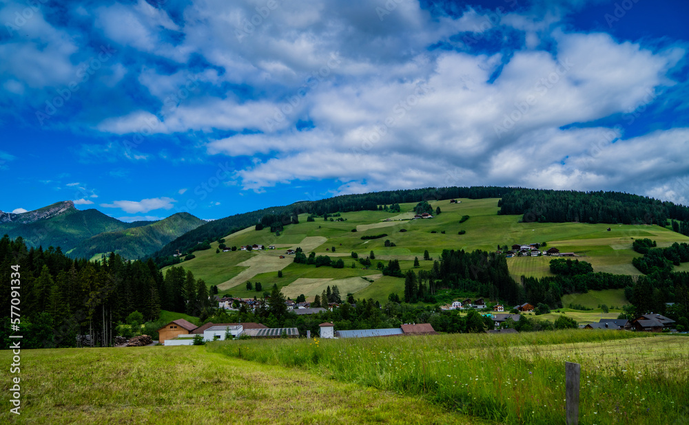 Rural mountain landscape in Italy in the Dolomites. Amazing bright colorful spring and summer landscape. Green blooming fields, wooded mountains and blue sky with clouds. Natural landscape, Europe.