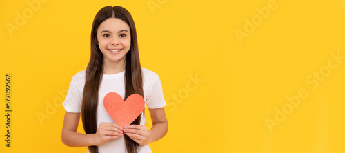 happy child with red heart on yellow background. Kid girl portrait with heart love symbol, horizontal poster. Banner header with copy space. © Olena