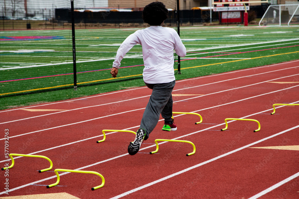 Fototapeta premium Rear view of a boy running fast over small hurdles on a track