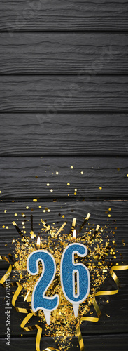 Number 26 blue celebration candle and gold confetti on dark wooden background. 26th birthday card. Anniversary and birthday concept. Vertical banner. photo