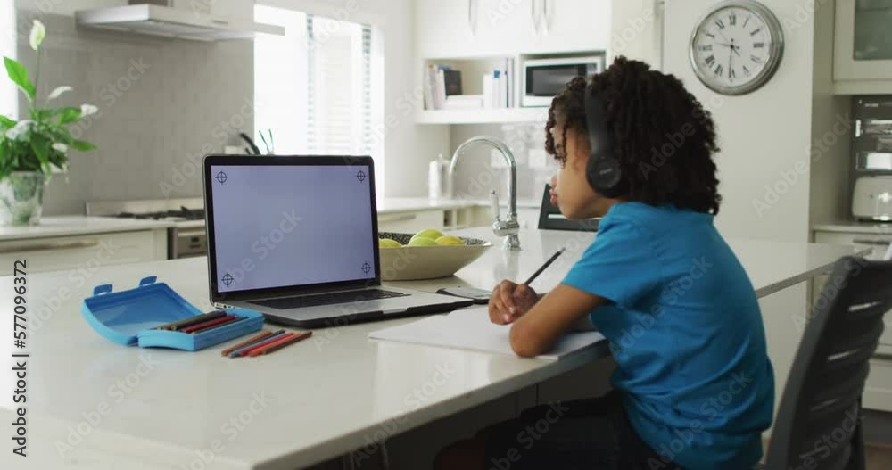 Happy biracial boy sitting at table using laptop with copy space and having online classes Happy biracial boy sitting at table using laptop with copy space and having online classes