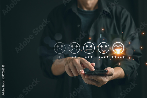 Businessman pressed the smile face emoticon on the virtual touch screen and give five star symbol on mobile to increase rating of products and customer service concept,selective focus.
