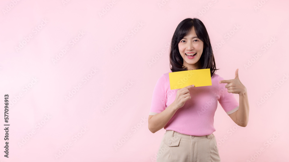 Portrait happy young woman model holding and showing blank space paper for advertisement information message poster with thumb up or point finger gesture isolated on pink pastel studio background. Portrait happy young woman model holding and showing blank space paper for advertisement information message poster with thumb up or point finger gesture isolated on pink pastel studio background.
