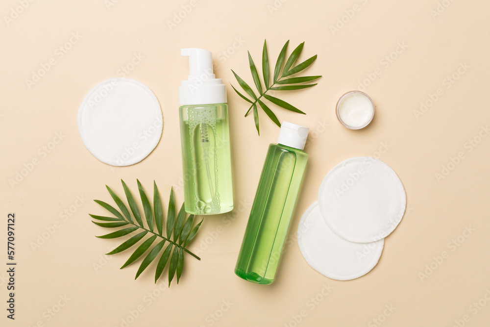 Foaming facial cleanser and micellar water with eco pads on color background, top view