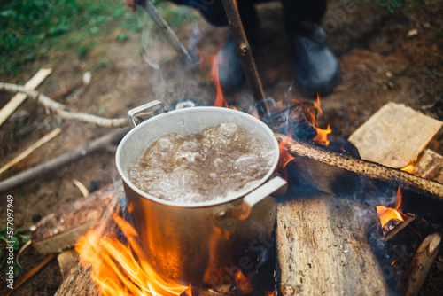 Preparing of cooking in woods outdoor. Brutal Cook soupwith meat or fish in hiking trip. Tourist warms up dinner in campfire. Camp on travel, place for bonfire. Survival in wild adventure in summer
