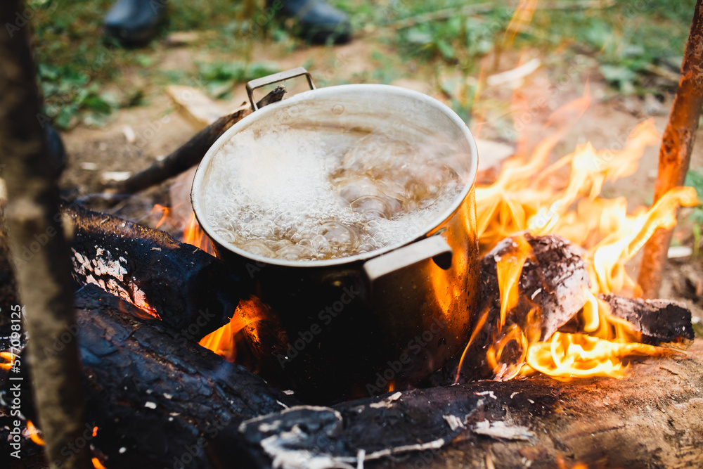 Preparing of cooking in woods outdoor. Brutal Cook soupwith meat or fish in hiking trip. Tourist warms up dinner in campfire. Camp on travel, place for bonfire. Survival in wild adventure in summer Preparing of cooking in woods outdoor. Brutal Cook soupwith meat or fish in hiking trip. Tourist warms up dinner in campfire. Camp on travel, place for bonfire. Survival in wild adventure in summer