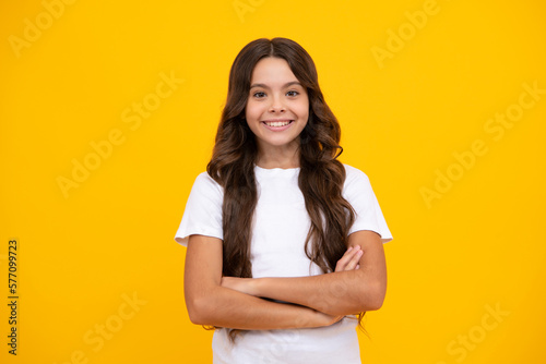 Portrait of young teenage girl standing with crossed arms against yellow background with copy space.