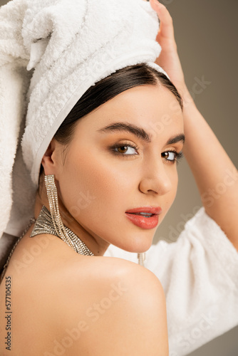 brunette woman with makeup touching white towel on head on grey background.