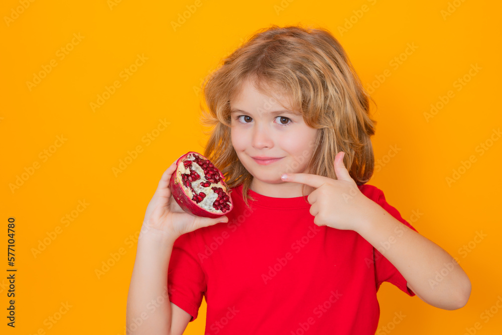 Vitamin and healthy fruits for kids. Kid hold red pomegranate in studio. Pomegranate fruit. Studio portrait of cute child with pomegranate isolated on yellow background with copy space. Vitamin and healthy fruits for kids. Kid hold red pomegranate in studio. Pomegranate fruit. Studio portrait of cute child with pomegranate isolated on yellow background with copy space.