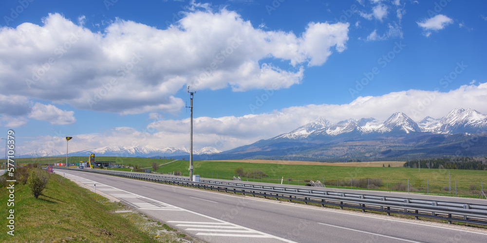 highway through the slovakian countryside, revealing a scenic view of the beautiful tatra mountains. the road leads through vast farmland, providing a beautiful backdrop for the journey