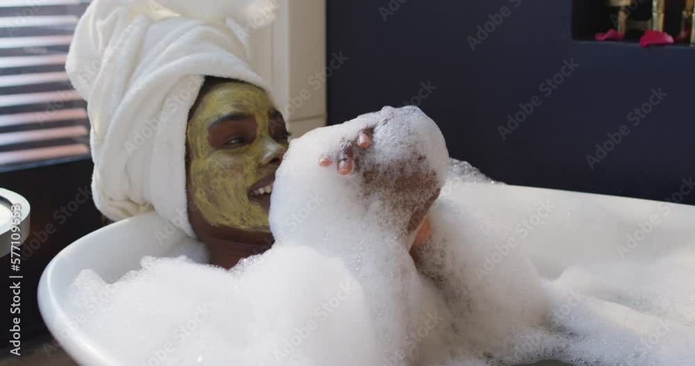 Smiling african american woman with towel and mask taking bath in bathroom Smiling african american woman with towel and mask taking bath in bathroom