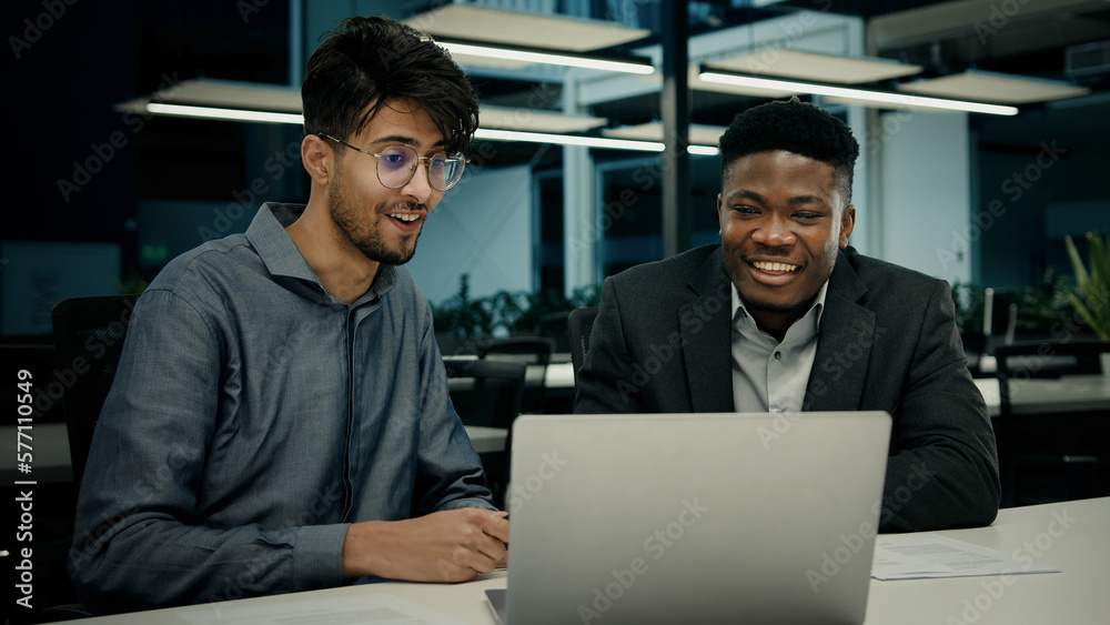 Fototapeta premium Male african indian colleagues workers men happy business people businessman laughing looking at computer screen having fun humor talking joke laugh watch funny video in office corporate partnership