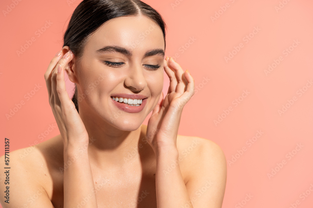 portrait of happy young woman with bare shoulders and flawless makeup smiling isolated on pink.