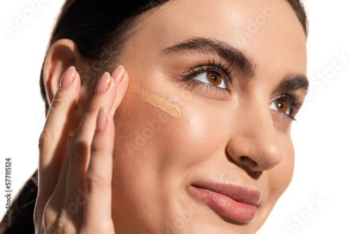 фотографія close up of young woman with soft skin applying makeup foundation on cheek with fingers isolated on white