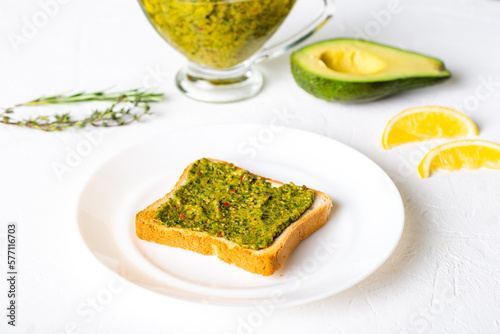 toast with avocado and chimichurri sauce on a white plate. Healthy vegetarian food. White background.
