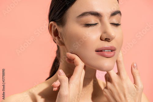 brunette woman with soft skin doing face massage isolated on pink.