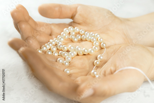 Woman hands holding pearl necklace on white background. Beads jewellery making process. Hobby handmade concept. Close-up. Selective focus. Blurred background.