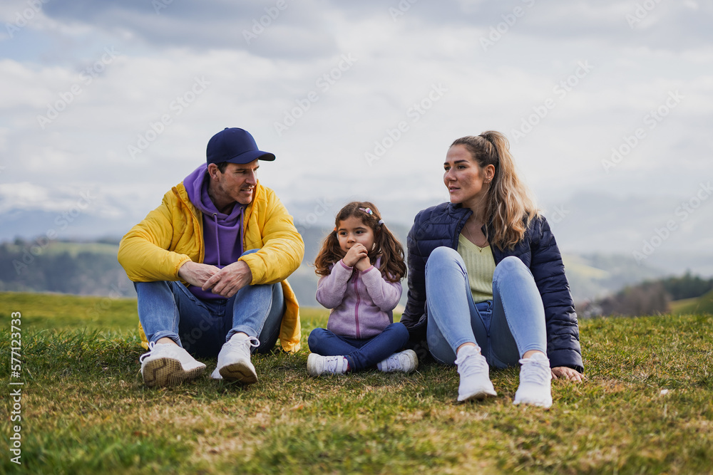 Happy family taking a break while sitting on meadow during trekking day in the nature - Mountains in the background - Travel concept Happy family taking a break while sitting on meadow during trekking day in the nature - Mountains in the background - Travel concept