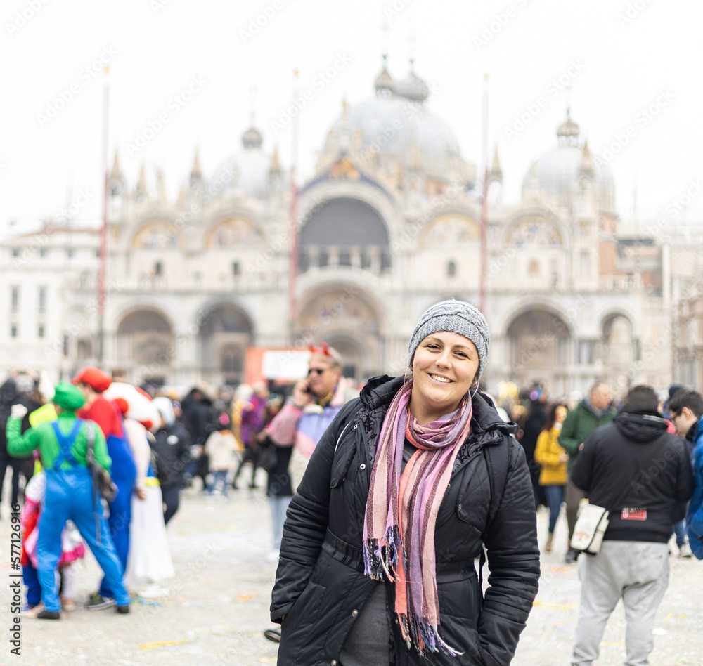 Woman in winter clothes and hands in pockets smiling at San Marco Square, Venice. Crowd and basilica on the background Woman in winter clothes and hands in pockets smiling at San Marco Square, Venice. Crowd and basilica on the background