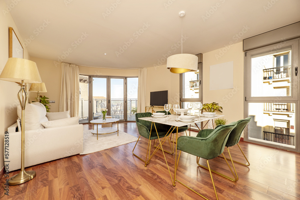 Fototapeta premium Dining room of a vacation rental home with a white marble dining table and gold metal legs, reddish wooden floors and a terrace with aluminum and glass doors