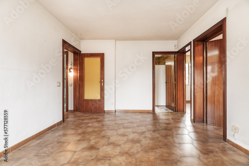 Living room of an empty apartment with cheap dark woodwork  white gotelet walls and brown tiled floors