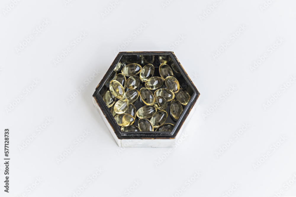 Fototapeta premium A hexagonal mother-of-pearl box with a black interior filled with pearls of a supreme liquid diet on a smooth white surface