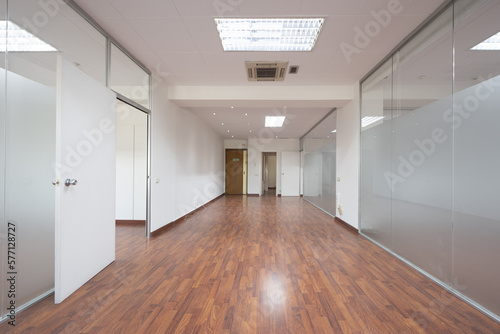 Empty offices with technical ceilings  white walls  reddish wooden floors and tempered glass partitions with transparent doors