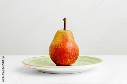 A lone ripe pear on a green plate on a plain white surface and a white background too
