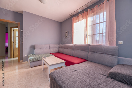 Furnished living room of a house with a stoneware floor and a perimeter sofa under a window and gray walls