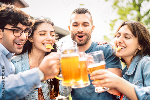 Young people drinking and toasting beer pints at brewery bar garden out doors - Food and beverage life style concept with guy and girls having fun together at happy hour - Bright vivid sunny filter