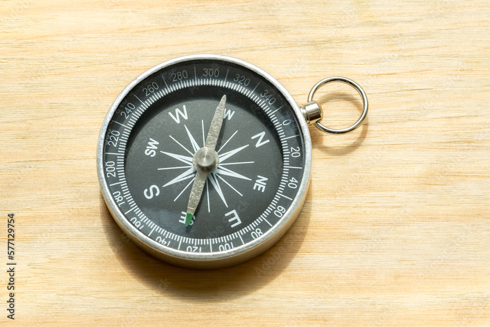 One simple small compass, wayfinding symbol world directions abstract concept, object closeup, natural sun light, laying on a wooden table, detail, up close. Navigation and pathfinding, search, travel One simple small compass, wayfinding symbol world directions abstract concept, object closeup, natural sun light, laying on a wooden table, detail, up close. Navigation and pathfinding, search, travel