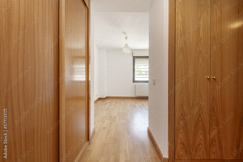 Hallway with a walk-in wardrobe with wooden doors and laminated oak floors and smooth white walls Hallway with a walk-in wardrobe with wooden doors and laminated oak floors and smooth white walls